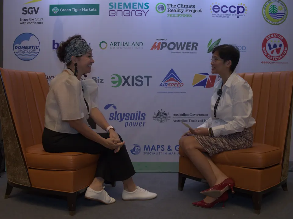 Two women recording an interview in front of the sponsor backdrop